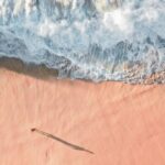 Beach Escape - Scenic Aerial Photo of a Sea Wave and Sandy Beach with Man Casting a Shadow