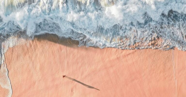 Beach Escape - Scenic Aerial Photo of a Sea Wave and Sandy Beach with Man Casting a Shadow