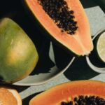 Vegetarians - Top view of halves of ripe papaya together with oranges and limes placed on green round dishes and green fabric on white background