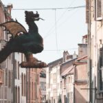 Myths And Legends - Sculpture of Graoully hanging in narrow avenue between residential buildings against cloudless sky on street of Metz in city of France
